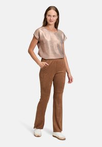 Haut à manches courtes à rayures bronze associé à un pantalon marron à texture lisse avec poches latérales, complété par des baskets blanches.
