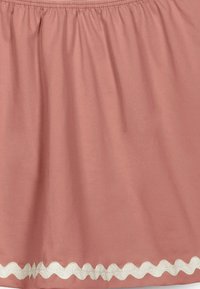 Falda de color rosa claro hecha de una tela suave, con una cintura fruncida y detalles de encaje blanco en zigzag en el dobladillo.