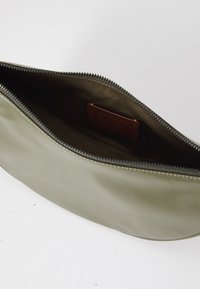 Borsa clutch in pelle verde oliva con una texture liscia, chiusura a zip e un'etichetta interna marrone. Il design è minimalista e rettangolare.