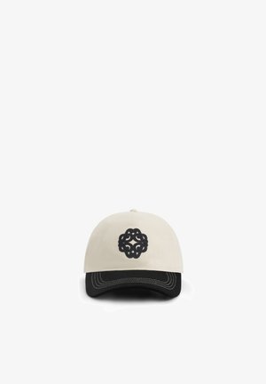 Beige and black baseball cap with black intricate circular emblem embroidered on front center above curved brim.