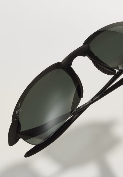 Black sunglasses with dark gray lenses, featuring a sleek design, rubber grips on the temples, and a metal logo on the upper frame.