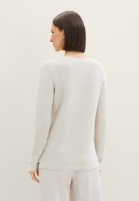 Pull en maille côtelée gris clair, manches longues, col rond, fentes latérales à l'ourlet, texture douce. La vue de dos montre une finition lisse et un design minimaliste.