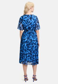 Niebieska sukienka plisowana z przezroczystymi rękawami w stylu motyla, ozdobiona kwiatowym wzorem. Zapięcie z tyłu na zamek błyskawiczny z wyraźną talią. Uzupełniona stylowymi szpilkami.