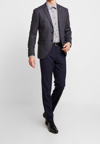 Navy tweed sako s klopovým límcem, doplněné vzorovanou šedou košilí na knoflíky, černým pásem a přizpůsobenými n�ámořnickými kalhotami.