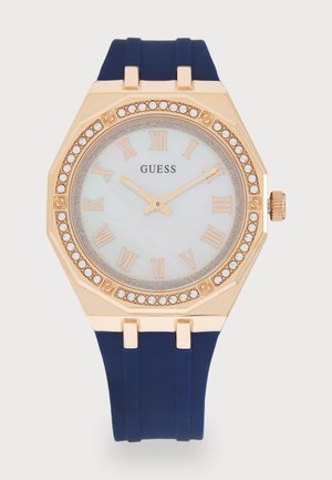Montre octogonale dorée avec un bracelet en silicone bleu, un cadran en nacre, des index en chiffres romains et des accents en cristal autour de la lunette.