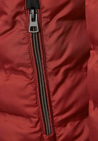 Rote gepolsterte Jacke mit einem kontrastierenden schwarzen Reißverschluss. Der Stoff wirkt glatt und glänzend und verfügt über gesteppte Abschnitte zur Isolierung.