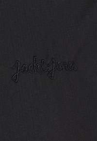 Tessuto nero con superficie testurizzata e una leggera lucentezza. Il nome del marchio "Jack & Jones" è ricamato in filo nero.