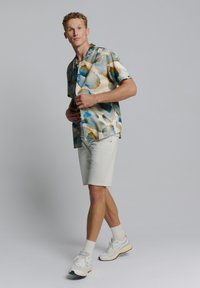 Korte mouwen shirt met een aquarelpatroon in blauw en beige, gecombineerd met licht beige shorts en witte sneakers. Gemaakt van gladde stof met een comfortabele pasvorm.