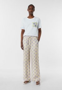 Jasnoniebieska bawełniana koszulka z wzorzystą kieszonką. Luźne, szerokie spodnie w kolorze żółtym, purpurowym i białym z geometrycznym wzorem.