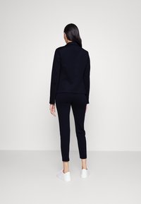 Completo sportivo blu navy composto da un blazer aderente e pantaloni affusolati, abbinato a sneakers bianche. Tessuto liscio e dettagli di design semplificati.