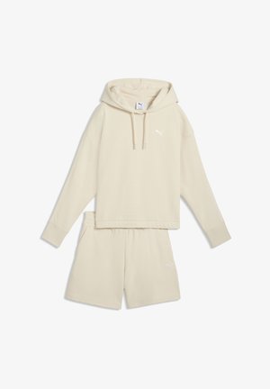Beżowa, oversize bluza z kapturem ze sznurkami oraz dopasowane beżowe szorty z elastyczną talią, oba z małymi logo Puma.
