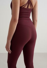 Burgundowy zestaw sportowy z prążkowanego materiału, składający się z dopasowanej bluzki crop z wieloma ramiączkami oraz legginsów z wysokim stanem. Miękka faktura, przylegający do ciała krój.