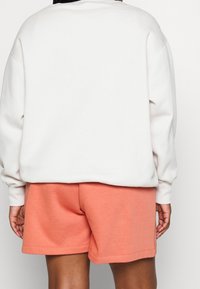 Gråmelerad sweatshirt med ribbade muddar, kombinerad med korallfärgade bomullsshorts med elastisk midja och fållade kanter.