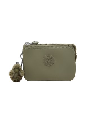 Pequeña bolsa con cremallera de color verde oliva con un parche redondo del logo y un llavero de mono peludo unido al tirador de la cremallera.