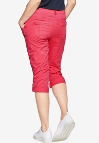 Pink capri pants with rolled cuffs and back pockets, made from a lightweight fabric. Worn with white sneakers.