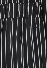 Tissu noir avec fines rayures blanches verticales et un détail de ceinture froncée.