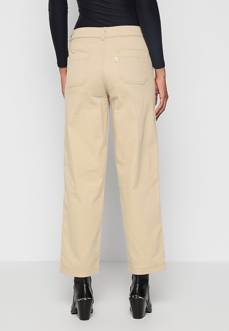 Pantalones de pierna ancha beige, hechos de algodón con una textura suave, que cuentan con dos bolsillos traseros y una cintura a media altura, combinados con botas de tacón negras.