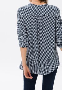 Blusa blu navy con motivo a pois bianchi, maniche lunghe, vestibilità comoda e dettaglio di piega al centro della schiena.