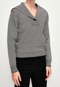 Pull rayé noir et blanc avec un large col marin, des manches longues et des poignets côtelés. Présente un détail de bouton au niveau du col.