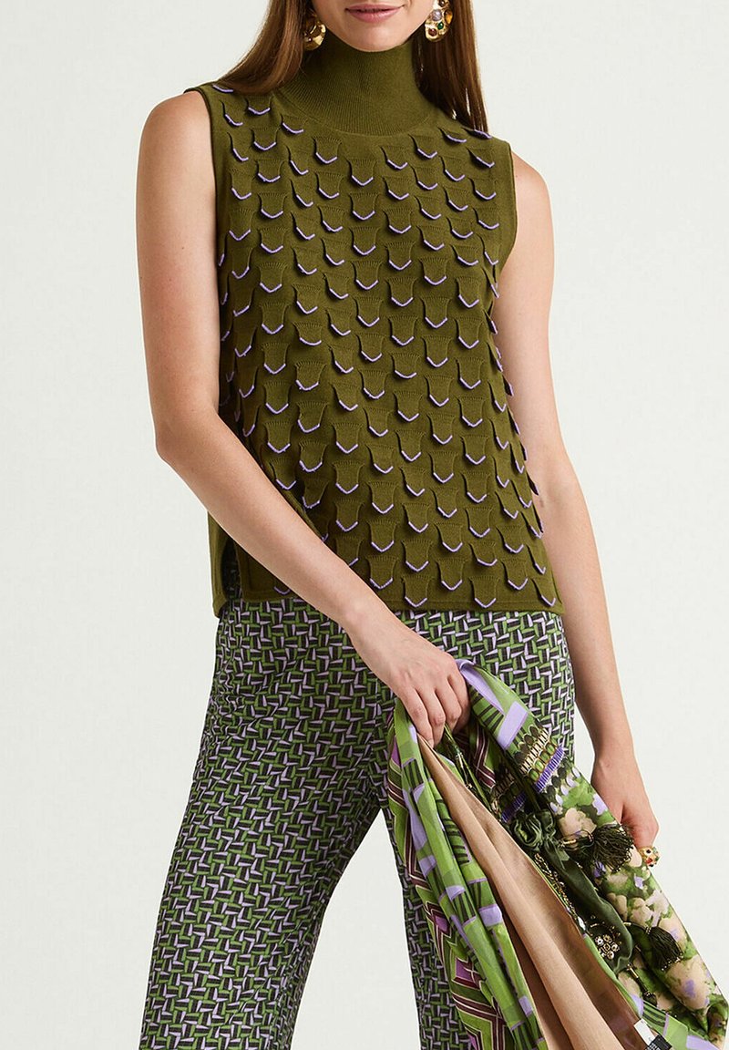 Haut vert sans manches avec un motif texturé et des accents violets. Associé à un pantalon à motifs verts et violets, tenant une écharpe multicolore.