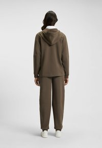 Brun hoodie med huva och matchande sweatpants, med avslappnad passform och slät textur, kombinerat med vita sneakers.