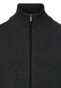 Nahaufnahme einer schwarzen, strukturierten Stoffjacke mit hohem Kragen und einem zentralen, vollständig geschlossenen schwarzen Reißverschluss.