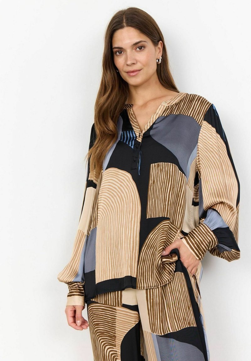 Flerfärgad blus med en blandning av geometriska mönster i beige, svart och blått, med ett mjukt tyg och knäppning vid halsen.