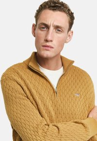 Maglione giallo senape con zip, caratterizzato da un motivo a diamante testurizzato, polsini e colletto a coste, con un piccolo logo sul petto.