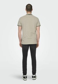 Khaki polo shirt met zwarte kraag en mouwaccenten, gecombineerd met donkere jeans en sneakers. Gladde textuur, korte mouwen, klassieke pasvorm.