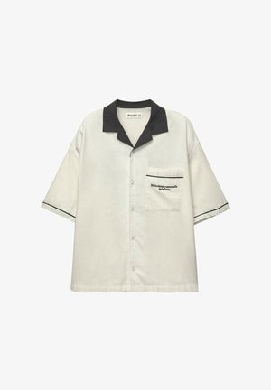 Kurzärmliges Hemd in hellbeige mit schwarzem Kragen. Verfügt über eine Brusttasche mit gesticktem Text und kontrastierenden schwarzen Abschlüssen an den Ärmeln.