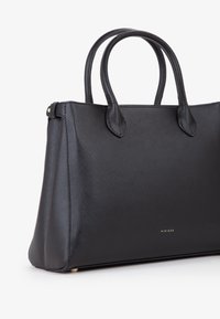 Borsa nera con design strutturato, texture liscia, manici corti e dettaglio del logo in oro. Presenta dei piedi in metallo alla base per maggiore stabilità.