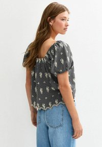 Black and white checked blouse with short puff sleeves, floral pattern, scalloped hem, and open back design, paired with light blue jeans.