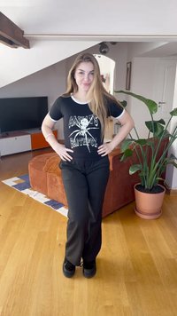 Musta t-paita, jossa valkoiset yksityiskohdat, spidgrafiikka ja teksti, yhdistetty mustiin housuihin ja mustiin kenkiin; sisätilat, joissa kasveja.