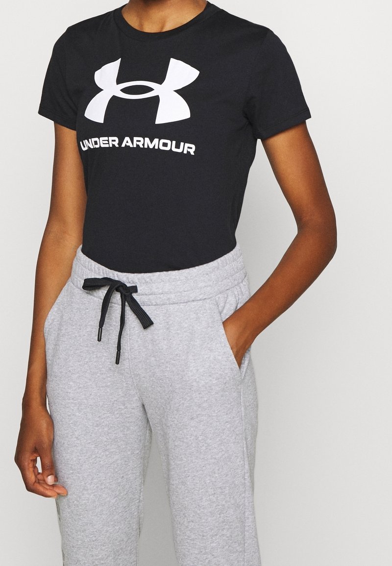 Svart bomullströja med vitt "UNDER ARMOUR"-logotyp, kombinerad med grå sweatshirtbyxor med elastisk midja och snörningsdetalj.