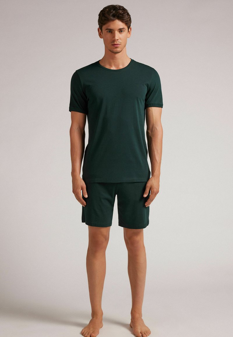 Dunkelgrünes Herren-T-Shirt mit kurzen Ärmeln und passender Shorts aus glattem Material. Schlichtes Design, Rundhalsausschnitt und knielange Shorts.