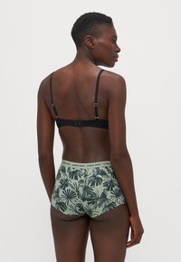 Black bra with adjustable straps, paired with green shorts featuring a black palm leaf pattern and an elastic waistband labeled "BJÖRN BORG."