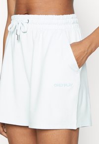 Frau in weißen Shorts mit elastischem Bund und Kordelzug, mit Hand in der Seitenasche, "ONLY PLAY" Logo am Saum.