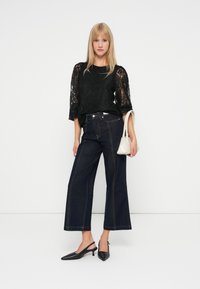 Czarna koronkowa bluzka z rękawami o długości trzech czwartych, wysoko taliowane ciemnoniebieskie szerokie spodnie dżinsowe oraz czarne, szpiczaste buty na obcasie typu slingback. Mała biała torebka.