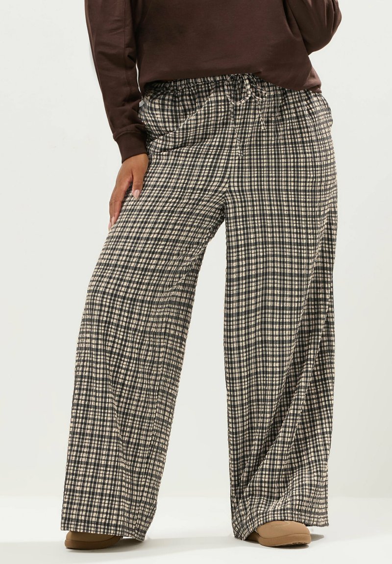 Breda byxor i ett svart och beige rutig mönster, gjorda av lättviktsmaterial med elastisk midja och dragsko.