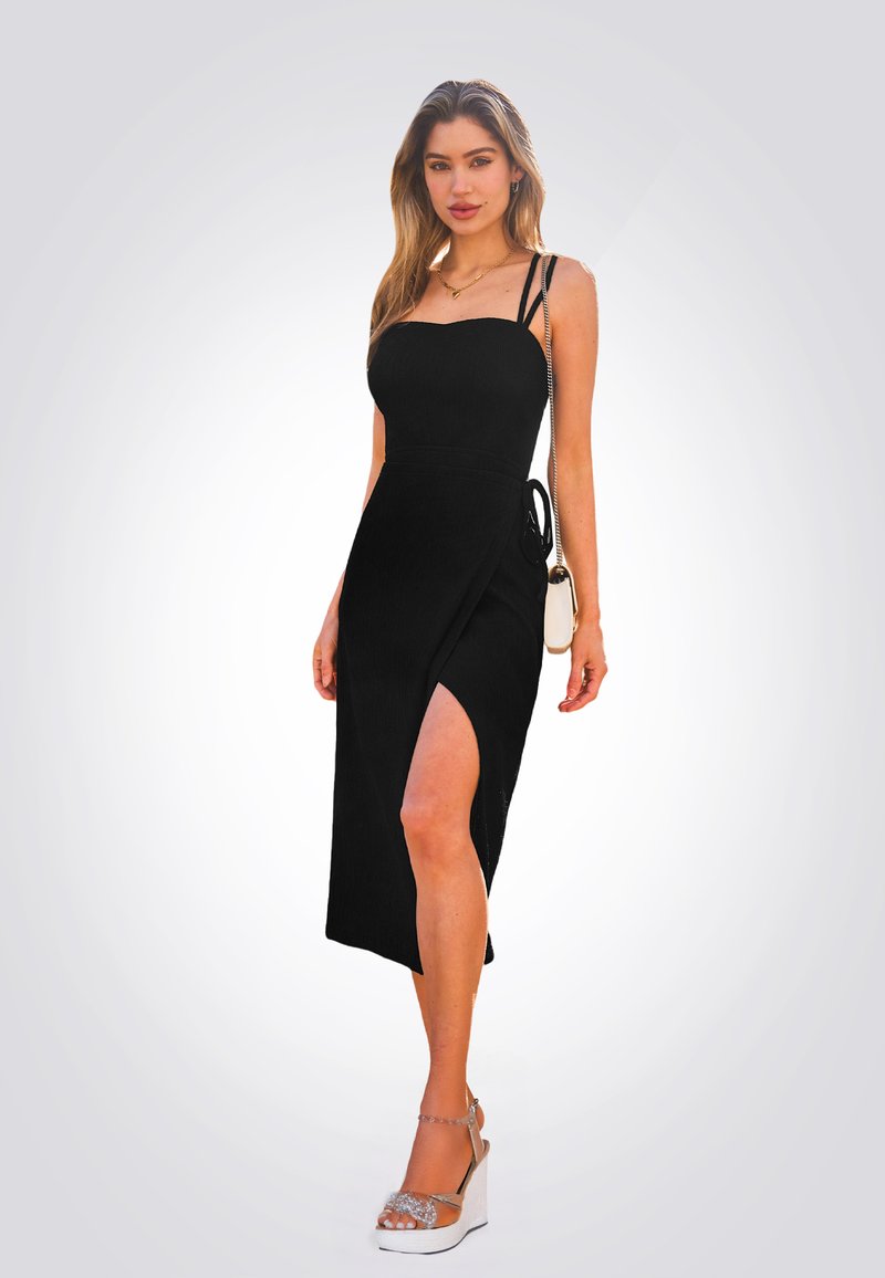 Schwarzes Midi-Kleid mit Spaghettiträgern, tailliertem Oberteil, seitlichem Schlitz und verstellbarem Band. Getragen mit Plateausandalen und einer kleinen Handtasche.