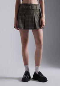 A plaid pleated skirt in earthy tones with a fitted waistband and buckle detail, paired with chunky black platform shoes and white socks.