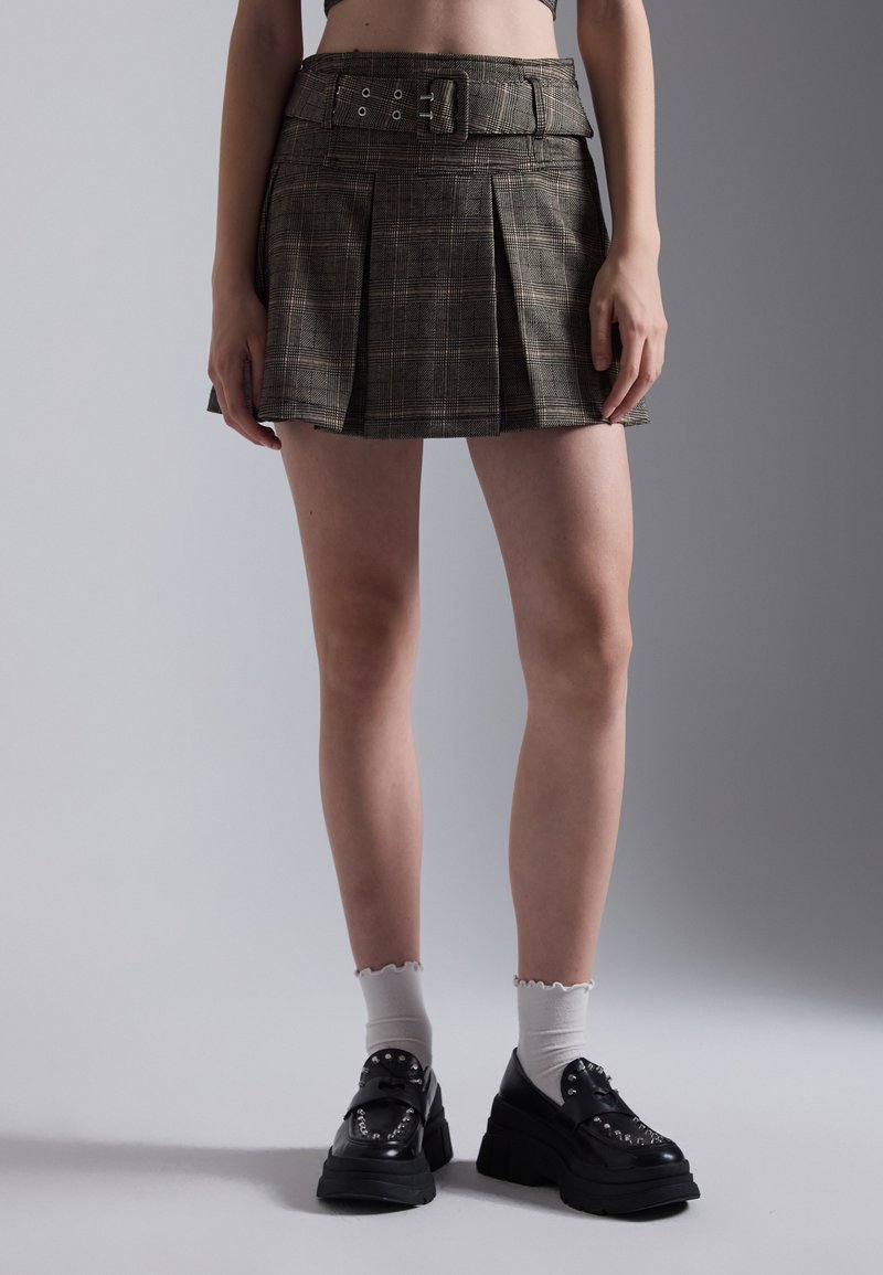 A plaid pleated skirt in earthy tones with a fitted waistband and buckle detail, paired with chunky black platform shoes and white socks.