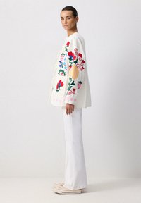 Valge tikandiga jakk, millel on värvilised lillemustrid, seotud esiseotud sulgemise ja suurte taskutega. Kombineeritud valgete laienevate pükste ja sneaksidega.