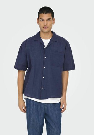 Chemise en lin bleu marine à manches courtes avec une poche poitrine, des boutons sur le devant et une coupe décontractée, assortie à un pantalon en denim clair.