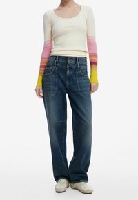 Maglietta a maniche lunghe con un corpo color crema chiaro e maniche a gradiente multicolore. Jeans in denim blu larghi con tasche frontali. Scarpe color crema.