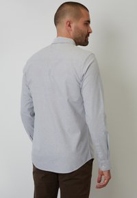Camisa de manga larga gris con cuello clásico, puños de botón y una textura suave. Presenta un dobladillo sutil y un diseño de yugo en la parte trasera.