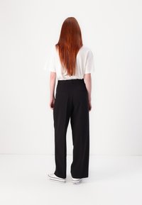 Black wide-leg trousers with a smooth texture, featuring two back pockets. Paired with a loose-fitting white t-shirt and white sneakers.