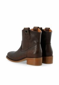 Par de botas de cuero marrón oscuro hasta el tobillo con tacones de madera, lengüetas de tirón y un sutil detalle de costura, mostradas desde ángulos traseros y laterales.