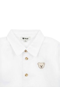 Camicia in cotone bianco con colletto a punta, dotata di tre bottoni dorati e un logo di un orso ricamato sul lato sinistro del petto.