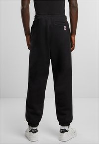 Schwarze Jogginghose mit elastischem Bund und Bündchen, Seitentaschen und einem kleinen Logopatch nahe der Gesäßtasche.